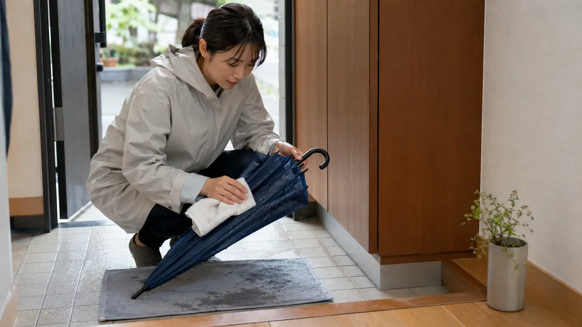 濡れた傘を乾かしてから収納 傘の収納前に濡れた傘をタオルで拭く日本人女性